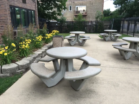 Several picnic tables outside the Armitage, in a closed off courtyard with a flowerbed nearby.