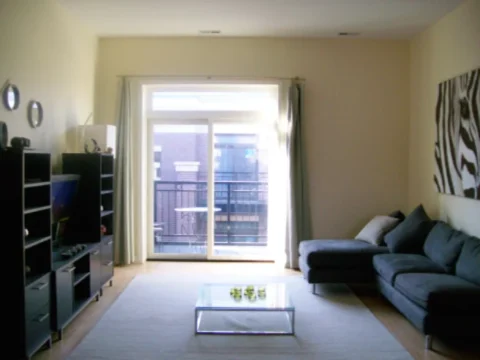 The living room of a Boulevard Court Apartment showing large sliding glass doors to a balcony, a couch, and entertainment setup.