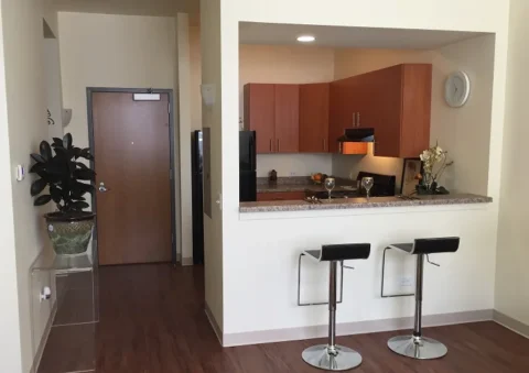 The kitchen has a bar with two bar stools, separated by a divider, as well as a black stove and fridge with wooden overhead cabinets.