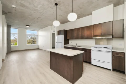 A modern kitchen with wooden cabinets, white appliances, and an open floor plan layout that combines with the living room.