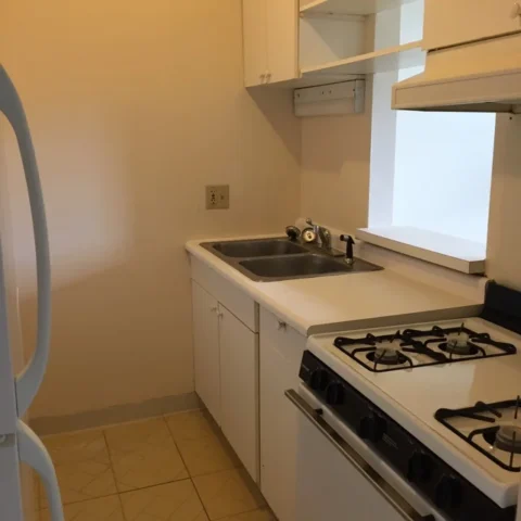 A galley kitchen with a double sink, four burner stove, and a window.