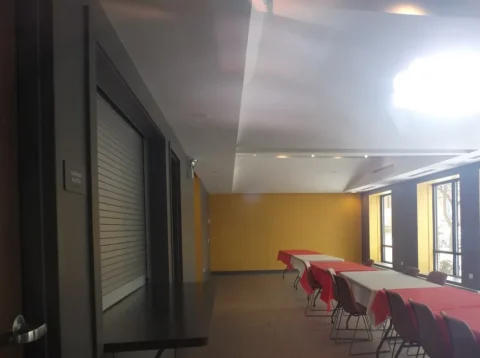 The community room has a yellow wall, several large windows, and many tables and chairs available.