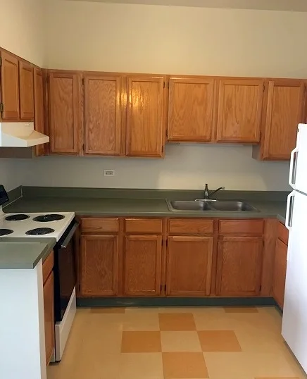 A kitchen with wooden cabinets, white appliances, and a double sink.